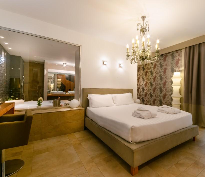 Camera moderna con letto matrimoniale, lampadario elegante e bagno a vista.